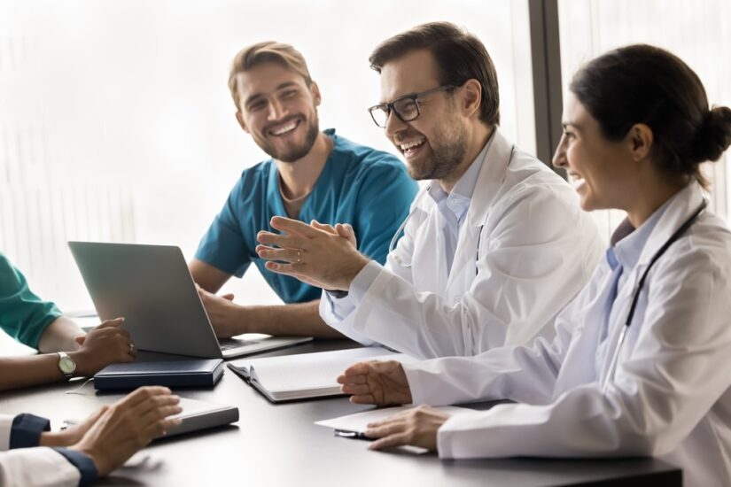 Happy multiethnic medical colleagues talking and laughing at meeting table, discussing successful doctor job, medical practice, work cases, having fun, enjoying networking